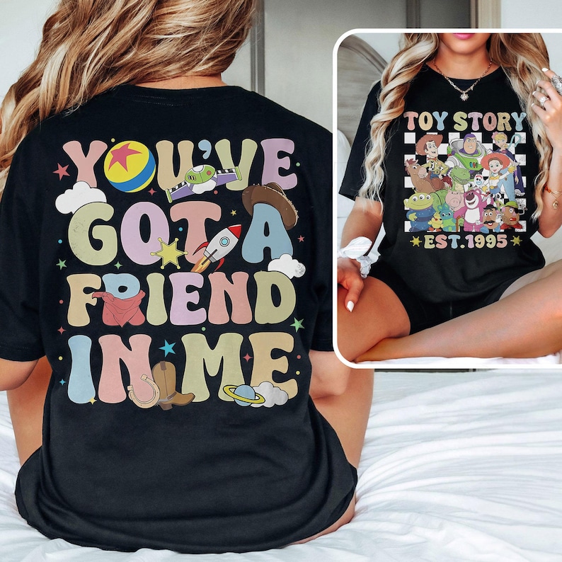 May include: Black t-shirt with a colorful retro graphic that says "You've Got a Friend in Me" with a cartoon rocket, cowboy hat, and stars. The back of the shirt has a checkered pattern with the text "Toy Story Est. 1995" and cartoon characters from the movie.