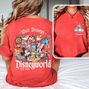 May include: Red t-shirt featuring a Disney World graphic on the back with Mickey, Minnie, Donald, Daisy, and Goofy. The front has a smaller graphic of a castle and the word "Custom". The shirt is a comfortable, casual style.