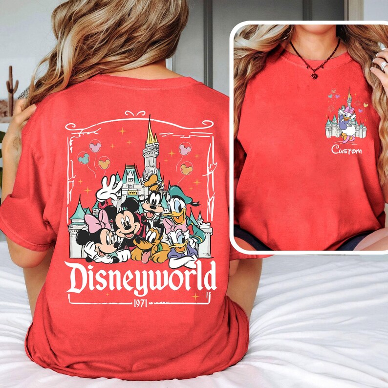 May include: Red t-shirt with a Disneyworld graphic on the back, featuring Mickey, Minnie, Donald, Daisy, Goofy, and Pluto in front of a castle. The front has a smaller castle graphic and Daisy Duck with the word "Custom".