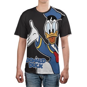 May include: Black t-shirt featuring a full-body graphic of Donald Duck in his classic outfit. The cartoon character is depicted with a blue sailor shirt, hat, and red bow tie. The words "DONALD DUCK" are printed in white and blue.