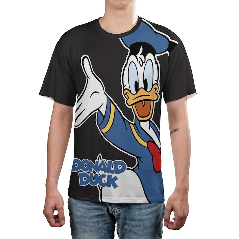 May include: Black t-shirt featuring a full-body graphic of Donald Duck in his classic outfit. The cartoon character is depicted with a blue sailor shirt, hat, and red bow tie. The words "DONALD DUCK" are printed in white and blue.
