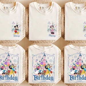 K&ouml;nnte beinhalten: Cremefarbene T-Shirts mit farbenfrohen Disney-Charakter-Designs. Einige Shirts zeigen Micky und Minnie Maus, andere haben eine Schlossgrafik mit verschiedenen Charakteren. Der Text enth&auml;lt "Daddy", "Mommy", "Custom" und "Birthday Squad".