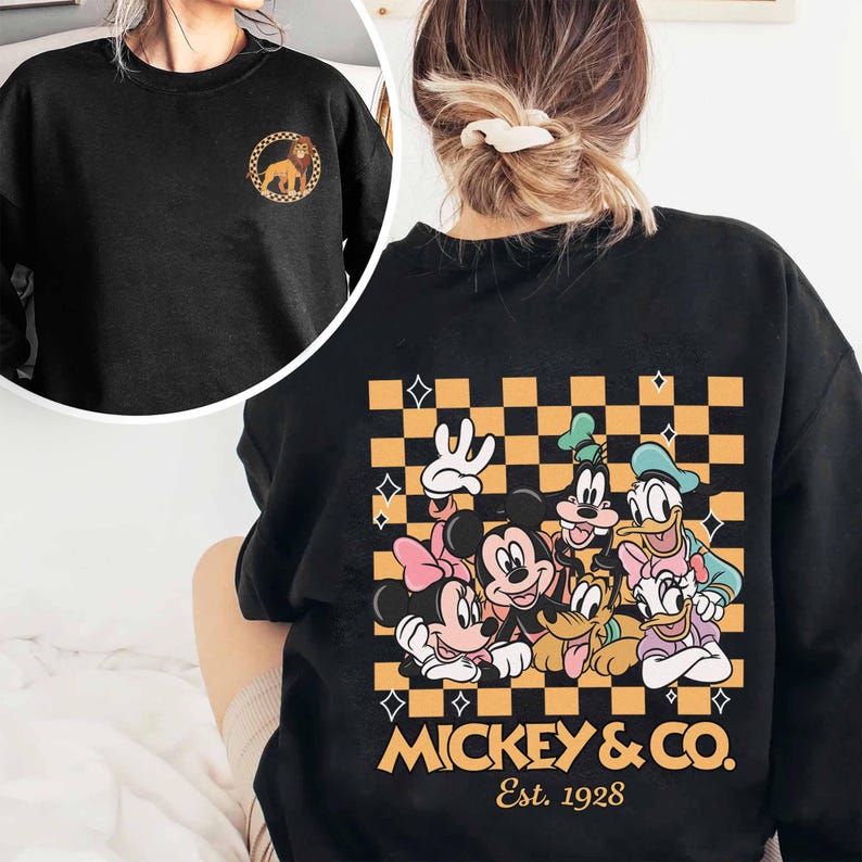 May include: Black sweatshirt with a checkered pattern and a graphic of Mickey Mouse and friends. The graphic includes Mickey Mouse, Minnie Mouse, Donald Duck, Goofy, Pluto, and Daisy Duck. The text "Mickey & Co. Est. 1928" is printed below the graphic.