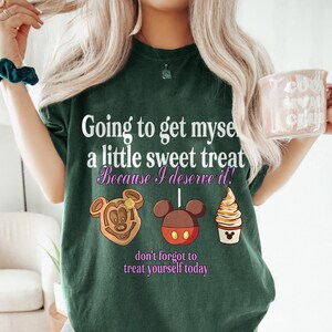 Puede incluir: Camiseta verde oscuro con el texto "Going to get myself a little sweet treat Because I deserve it!" e im&aacute;genes de dibujos animados de un gofre, una piruleta de Mickey Mouse y un helado de crema. La frase "don't forget to treat yourself today" tambi&eacute;n est&aacute; impresa en la camiseta.