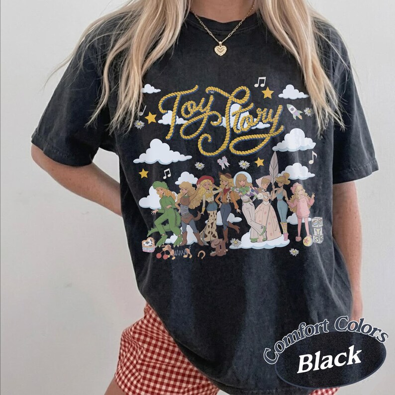 May include: A black short-sleeve t-shirt featuring a graphic print of various characters from Toy Story. The design includes the text Toy Story in a yellow rope-style font, surrounded by white clouds, stars, musical notes, and a small rocket ship.