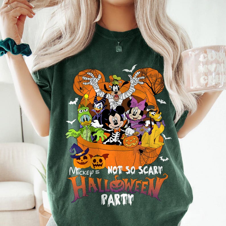 May include: Dark green t-shirt featuring a Halloween-themed graphic. The design includes Mickey Mouse and friends dressed in costumes, with the text "Mickey's Not So Scary Halloween Party" in orange and purple. Bats and pumpkins are also included.