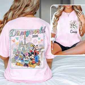 Pu&ograve; includere: T-shirt rosa chiaro con un design Disney World 2026 sul retro, con vari personaggi dei cartoni animati e un castello. La tasca anteriore ha una grafica di Olaf e il nome "Carley".