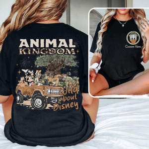 May include: Black t-shirt featuring a graphic of Mickey Mouse, Goofy, and Donald Duck in a brown jeep with the text "ANIMAL KINGDOM" and "Wild about Disney". The shirt also has a small graphic of Donald Duck with the text "Custom Name".