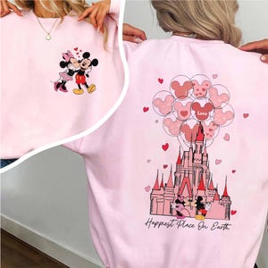 May include: Pink sweatshirt featuring Mickey and Minnie Mouse. The front shows the couple embracing, while the back displays a castle, Mickey Mouse balloons, and the text "Happiest Place On Earth."