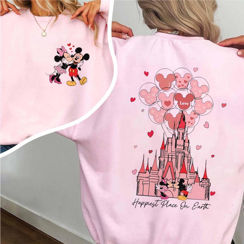 May include: Pink sweatshirt featuring Mickey and Minnie Mouse. The front shows the couple embracing, while the back displays a castle, Mickey Mouse balloons, and the text "Happiest Place On Earth."