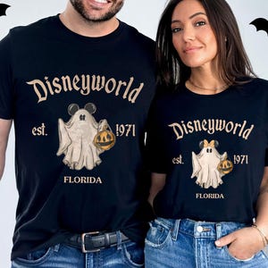 May include: Black t-shirts with a Disneyworld Halloween design. The shirts feature the text "Disneyworld est. 1971 FLORIDA" and a cartoon ghost holding a jack-o'-lantern. Bats are in the background.