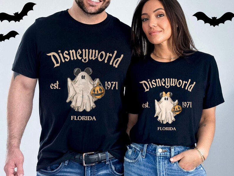 May include: Black t-shirts with a Disneyworld Halloween design. The shirts feature the text "Disneyworld est. 1971 FLORIDA" and a cartoon ghost holding a jack-o'-lantern. Bats are in the background.