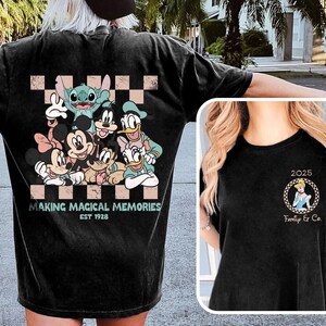 以下が含まれることがあります： ミッキーマウス、ドナルドダック、スティッチなどのディズニーキャラクターのカラフルなグラフィックが特徴の黒いTシャツ。「MAKING MAGICAL MEMORIES EST 1928」の文字も含まれています。右側の小さな画像にはシンデレラのグラフィックが表示されています。