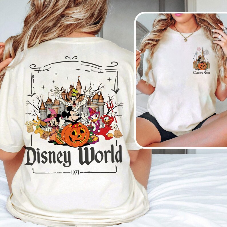 May include: Cream-colored t-shirt featuring a Halloween-themed Disney World graphic. The design includes Mickey Mouse, Minnie Mouse, Donald Duck, and other characters in costumes, with a pumpkin and castle. The text "Disney World - 1971" is also included.