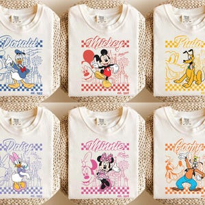 May include: Six off-white t-shirts featuring Disney characters: Donald Duck, Mickey Mouse, Pluto, Daisy Duck, Minnie Mouse, and Goofy. Each shirt has a character graphic, name, and "est. 1955" text. The designs are set against a checkered background.