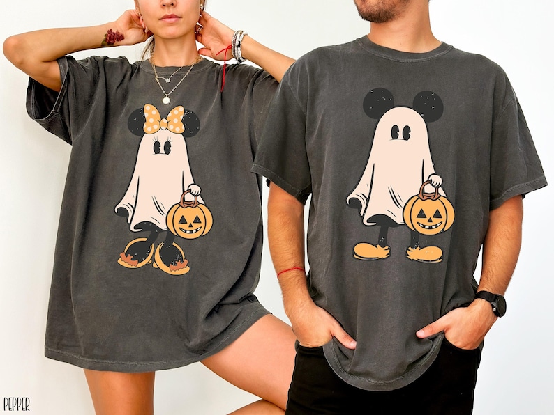 May include: Two black t-shirts with a ghost Mickey Mouse and Minnie Mouse design. The ghosts are holding jack-o'-lanterns. The shirts are a distressed charcoal color.