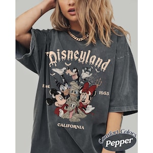 May include: A charcoal gray t-shirt featuring a graphic print of Disney characters including Mickey Mouse, Minnie Mouse, Donald Duck, and Goofy in Halloween costumes. The text reads Disneyland Est 1955 California. The shirt has a faded, worn-in look.