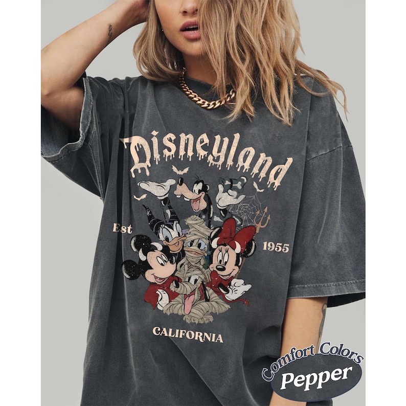 May include: A charcoal gray t-shirt featuring a graphic print of Disney characters including Mickey Mouse, Minnie Mouse, Donald Duck, and Goofy in Halloween costumes. The text reads Disneyland Est 1955 California. The shirt has a faded, worn-in look.