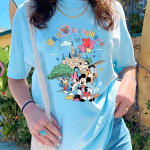 May include: A light blue t-shirt with a graphic print of Mickey Mouse and friends in front of Cinderella's Castle. The text "Walt Disney World" is printed in a colorful font.
