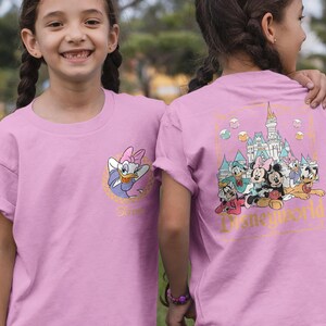 May include: Pink t-shirt with a graphic of Disney characters in front of Cinderella's Castle. The back of the shirt features a graphic of Disney characters with the text "Disney World".