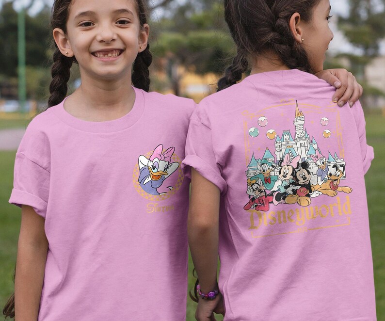 May include: Pink t-shirt with a graphic of Disney characters in front of Cinderella's Castle. The back of the shirt features a graphic of Disney characters with the text "Disney World".