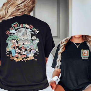 Puede incluir: Camiseta negra con un gr&aacute;fico colorido de personajes de Disney y el texto "Walt Disney World". El dise&ntilde;o incluye a Mickey Mouse, Minnie Mouse, el Pato Donald y Goofy frente a un castillo. Una camiseta m&aacute;s peque&ntilde;a muestra un dise&ntilde;o personalizado.