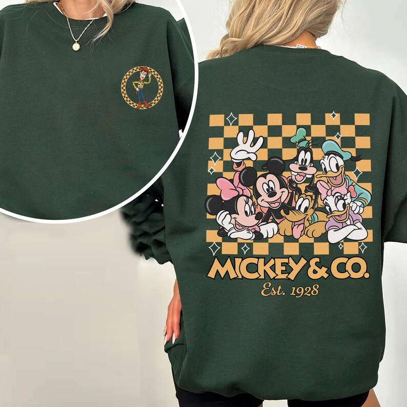 May include: A dark green sweatshirt with a Mickey Mouse and friends graphic on the back. The graphic features Mickey Mouse, Minnie Mouse, Donald Duck, Goofy, and Pluto. The graphic is on a checkered background with gold stars. The text "Mickey & Co. Est. 1928" is below the graphic.
