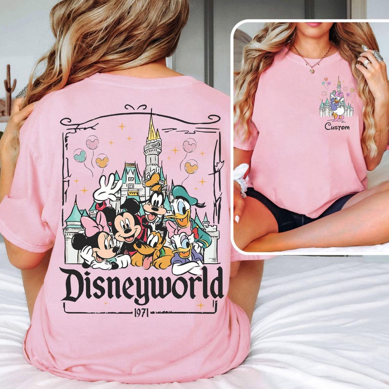 May include: Pale pink t-shirt with a Disneyworld graphic on the back, showcasing Mickey, Minnie, Donald, Goofy, and Pluto in front of a castle. The front has a smaller graphic with Daisy Duck and a castle. The word "Custom" is below the graphic.