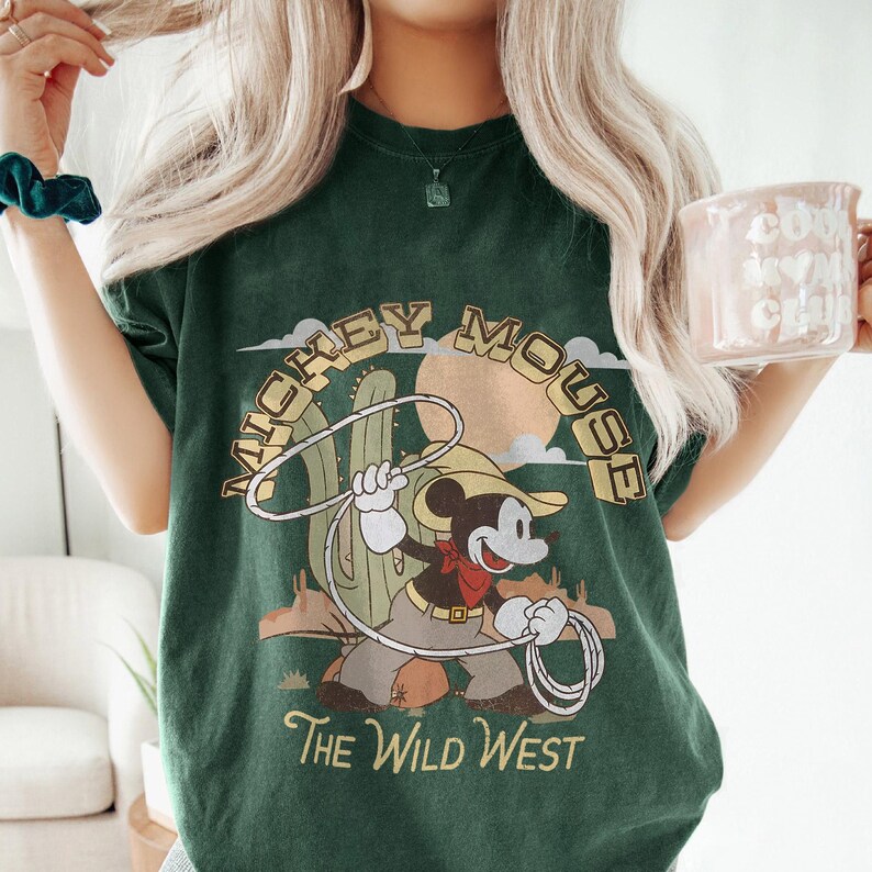 May include: Dark green t-shirt with a vintage Mickey Mouse cowboy graphic, holding a lasso against a desert backdrop. The text "MICKEY MOUSE" is arched above the image, with "The Wild West" below.
