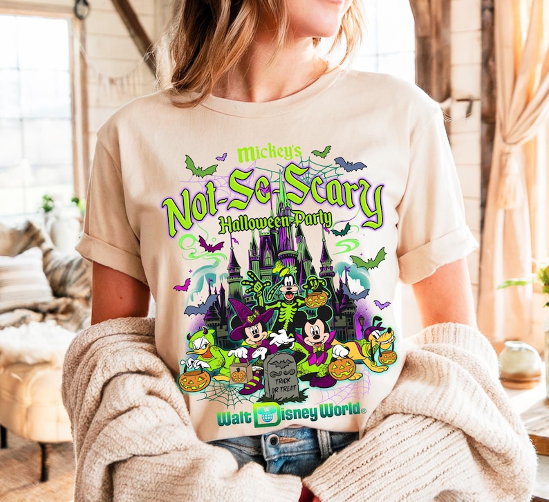 May include: Beige t-shirt with a vibrant graphic promoting Mickey's Not-So-Scary Halloween Party at Walt Disney World. The design showcases Mickey, Minnie, Donald, Goofy, and Pluto in Halloween attire, set against a spooky castle scene.