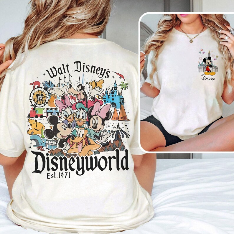 May include: Cream-colored t-shirt featuring a colorful Disneyworld graphic on the back with Mickey Mouse, Donald Duck, and other characters. The front of the shirt has a smaller Mickey Mouse graphic with the word "Daddy" below.