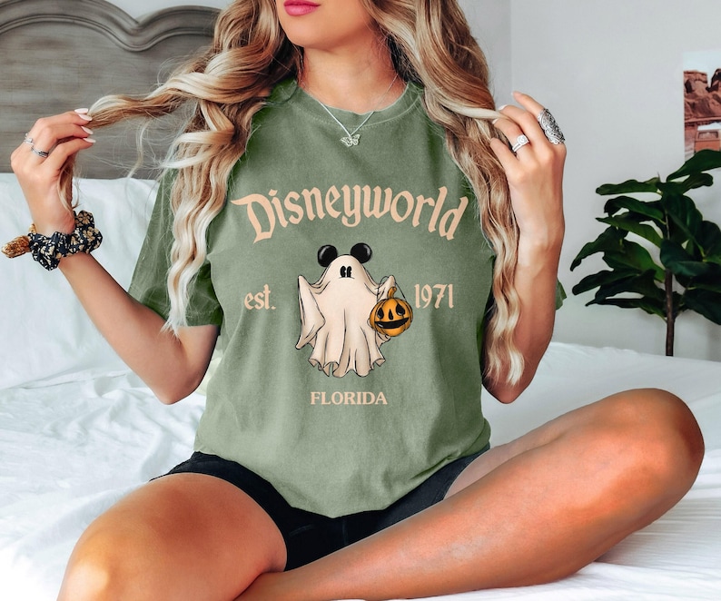 Op de afbeelding: Groen T-shirt met een vintage-stijl afbeelding van een geest die een pompoen vasthoudt. De tekst op het shirt luidt "Disneyworld est. 1971 Florida".