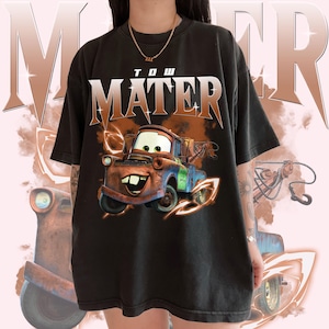 May include: Black t-shirt with a graphic of Tow Mater from the Cars movie. The graphic is in orange, red, blue, and green. The text "Tow Mater" is printed in white on the shirt.