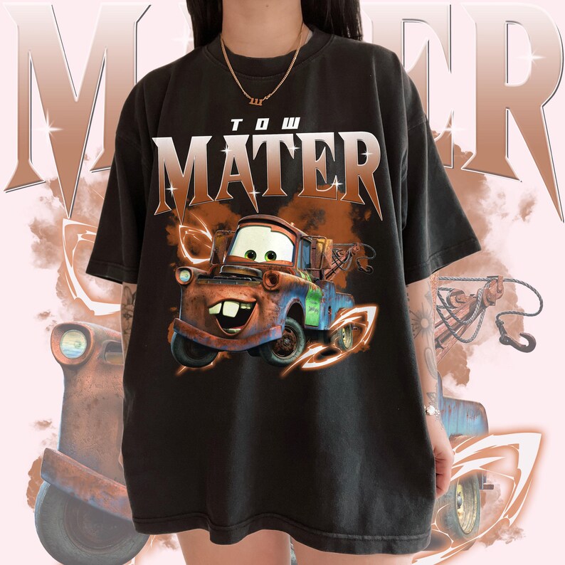 May include: Black t-shirt with a graphic of Tow Mater from the Cars movie. The graphic is in orange, red, blue, and green. The text "Tow Mater" is printed in white on the shirt.