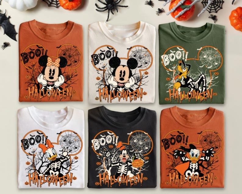 Pode incluir: Seis camisetas com tema de Halloween com personagens da Disney. Cada camisa tem um design de personagem com tema de esqueleto, a palavra "BOO!!" e o texto "HALLOWEEN". As cores incluem laranja, branco, preto e verde.