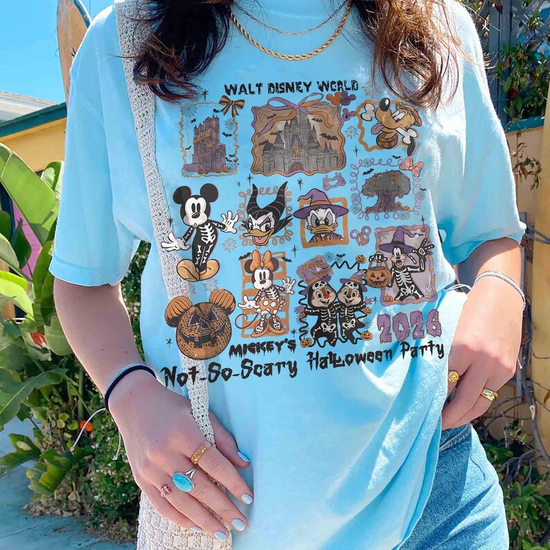 May include: Light blue t-shirt featuring a graphic of Disney characters in Halloween costumes. The shirt includes the text "Walt Disney World" and "Mickey's Not-So-Scary Halloween Party 2026".