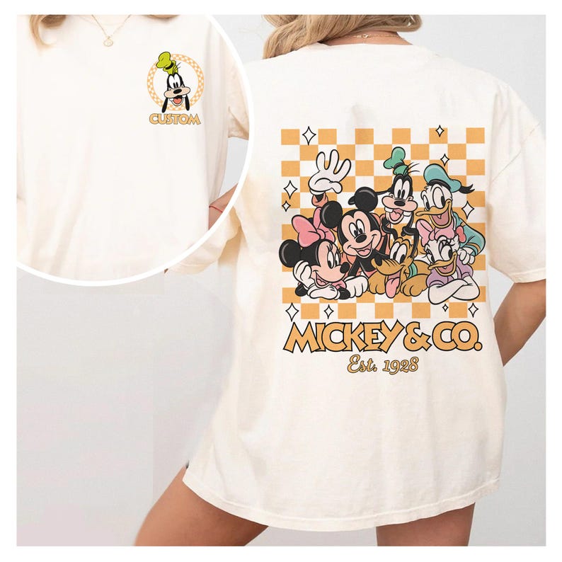 May include: A white t-shirt with a checkered pattern and a graphic of Mickey Mouse and his friends. The graphic includes Mickey Mouse, Minnie Mouse, Donald Duck, Goofy, Pluto, and Daisy Duck. The text "MICKEY & CO. Est. 1928" is printed below the graphic.