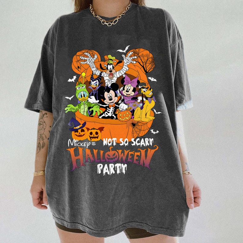 May include: Dark gray t-shirt featuring a Halloween-themed graphic. The design includes Mickey Mouse, Minnie Mouse, Goofy, Donald Duck, and other Disney characters in a pumpkin. Text on the shirt reads "Mickey's Not So Scary Halloween Party."