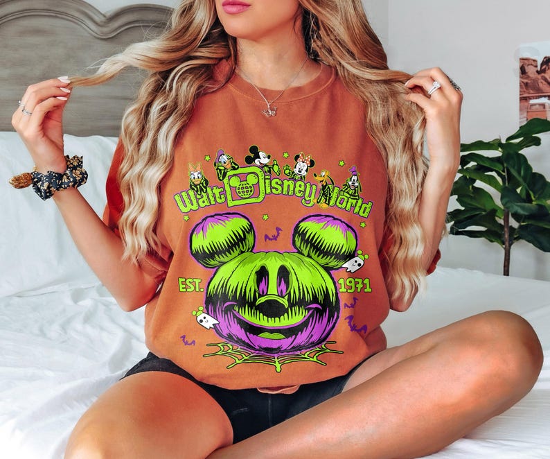 May include: Orange t-shirt featuring a Halloween-themed Walt Disney World design. The graphic includes a green and purple Mickey Mouse pumpkin, the text "Walt Disney World," and the year "1971."