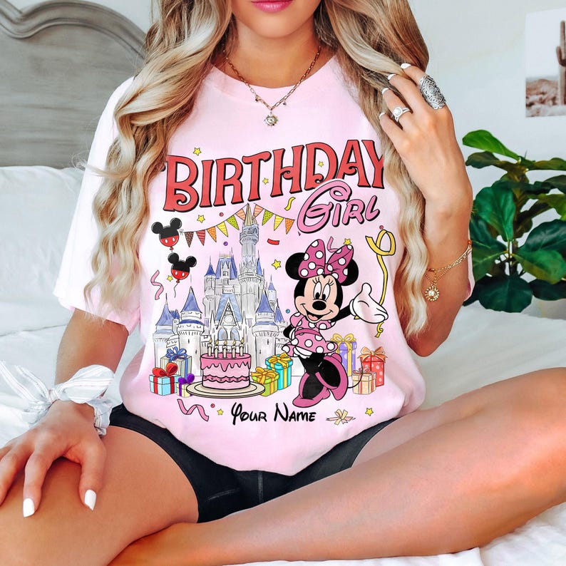 K&ouml;nnte beinhalten: Hellrosa T-Shirt mit farbenfroher Grafik von Minnie Mouse, einem Schloss und dem Text "BIRTHDAY GIRL". Das Design beinhaltet Ballons, Geschenke und die M&ouml;glichkeit, einen Namen hinzuzuf&uuml;gen. Ein festliches und lustiges Design.