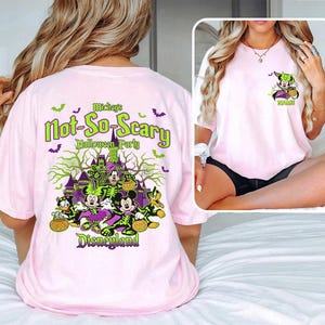 May include: Pink t-shirt featuring a Halloween-themed graphic. The design includes Mickey and Minnie Mouse in costume, a haunted castle, bats, and the text "Mickey's Not-So-Scary Halloween Party Disneyland."