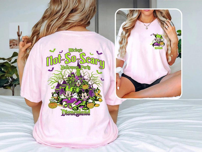 May include: Pink t-shirt featuring a Halloween-themed graphic. The design includes Mickey and Minnie Mouse in costume, a haunted castle, bats, and the text "Mickey's Not-So-Scary Halloween Party Disneyland."