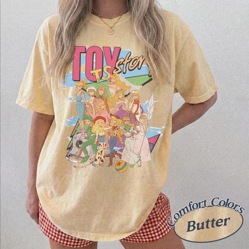 May include: A butter yellow short-sleeve t-shirt featuring a graphic print of various animated characters and the text Toy Story. The design includes a colorful collage of figures in a retro style, set against a light blue and geometric background.