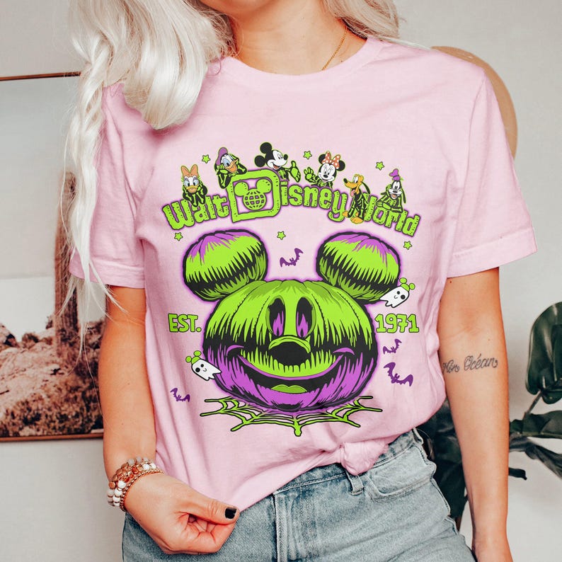 May include: Pink t-shirt featuring a Halloween-themed Mickey Mouse pumpkin design with the text "Walt Disney World" and "EST. 1971". The graphic includes bats, ghosts, and a spiderweb.