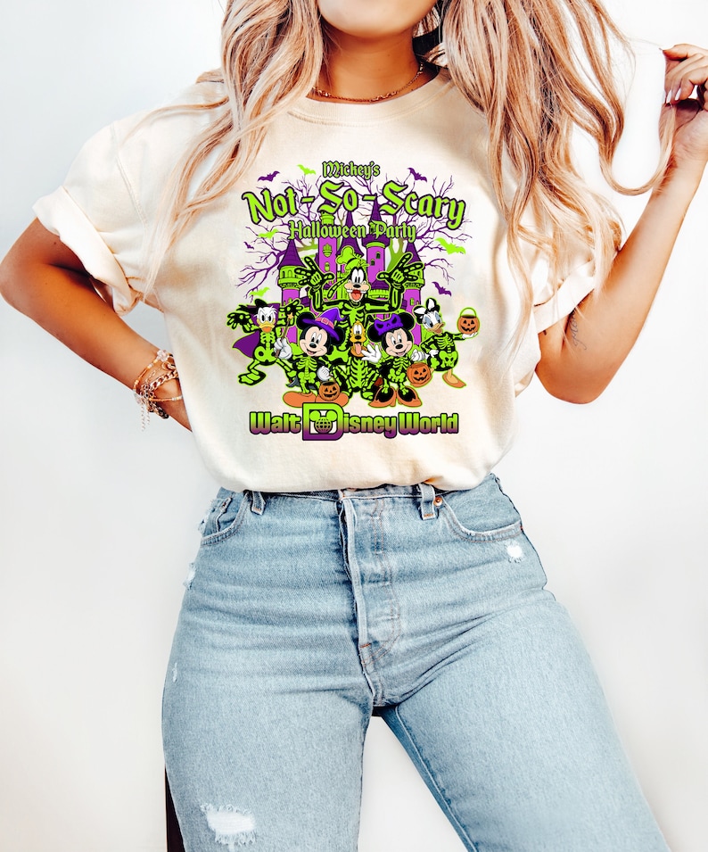 May include: Cream-colored t-shirt featuring a Halloween-themed graphic. The design includes Disney characters dressed in skeleton costumes, a haunted castle, and the text "Mickey's Not-So-Scary Halloween Party" and "Walt Disney World".