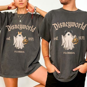 May include: Dark gray t-shirts with a vintage-style Disneyworld graphic featuring a ghost holding a jack-o'-lantern. The text reads "Disneyworld est. 1971 FLORIDA". The ghost has Mickey Mouse ears and a bow. The shirts are oversized.