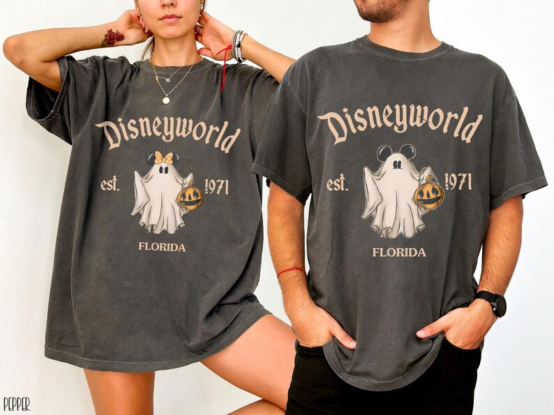 May include: Dark gray t-shirts with a vintage-style Disneyworld graphic featuring a ghost holding a jack-o'-lantern. The text reads "Disneyworld est. 1971 FLORIDA". The ghost has Mickey Mouse ears and a bow. The shirts are oversized.