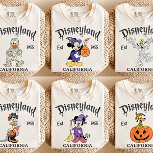 May include: Six off-white t-shirts with Disneyland graphics. Each shirt features a different cartoon character dressed in Halloween costumes. The Disneyland logo is in a spooky font, with "Est 1955 CALIFORNIA" below.