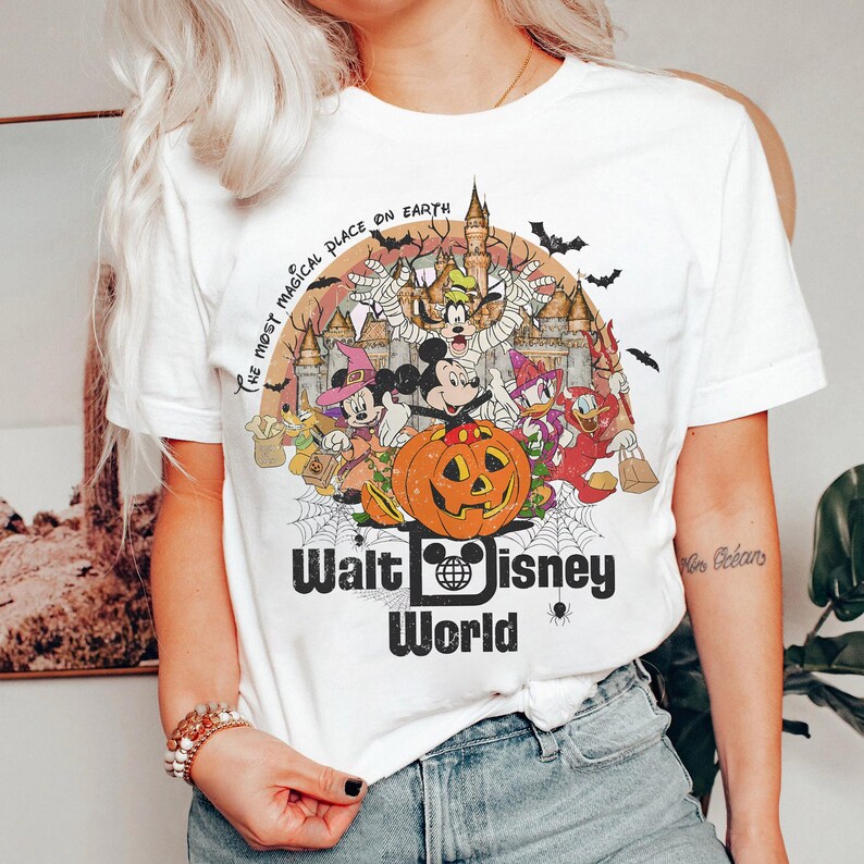 May include: White t-shirt with a vintage-style graphic of Mickey Mouse and other Disney characters in Halloween costumes. The text "The most magical place on Earth" and "Walt Disney World" are printed on the shirt.