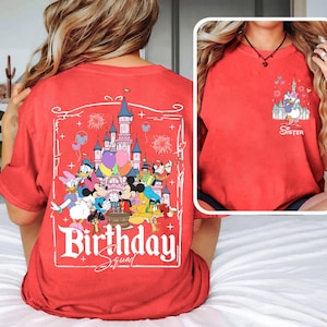 K&ouml;nnte beinhalten: Rotes T-Shirt mit einem Disney-Schloss und Figuren, darunter Micky und Minnie Maus, Donald Duck und Goofy. Auf der R&uuml;ckseite des Shirts steht "Birthday Squad". Auf der Vorderseite des Shirts befindet sich ein kleineres Bild des Schlosses und das Wort "Sister".